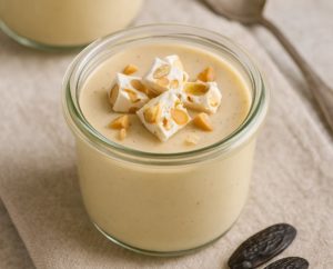 Verrine de crème dessert à la fève tonka avec morceaux de nougat, posée sur une serviette beige avec fèves tonka en décor