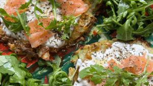 Tarte de pommes de terre écrasées garnie de saumon fumé, fromage frais et roquette